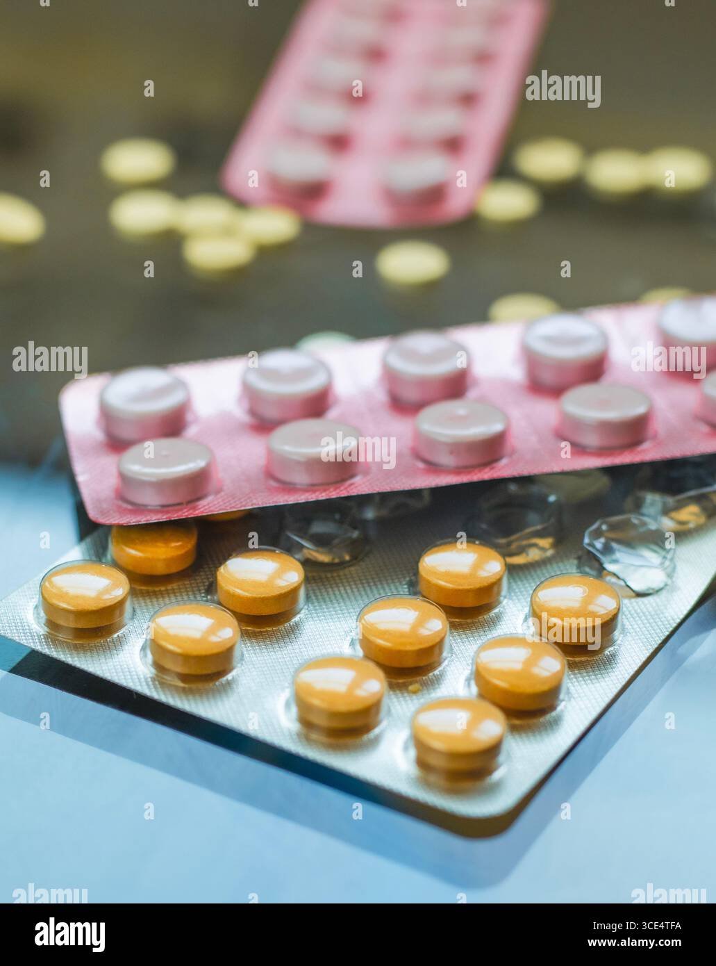 Le confezioni blister di varie pillole, incluse quelle arancioni e rosa, sono esposte contro una superficie riflettente. Alcune pillole gialle sfuse sono sparse in t Foto Stock