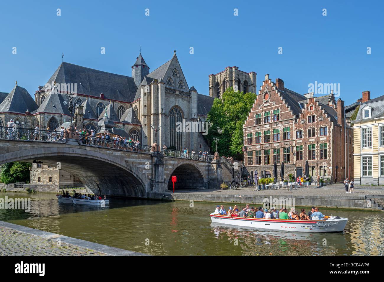 Tour in barca con i turisti sul fiume Lys / Leie lungo il Korenlei, il ponte di San Michele e la chiesa nella città di Gand in estate, nelle Fiandre orientali, in Belgio Foto Stock