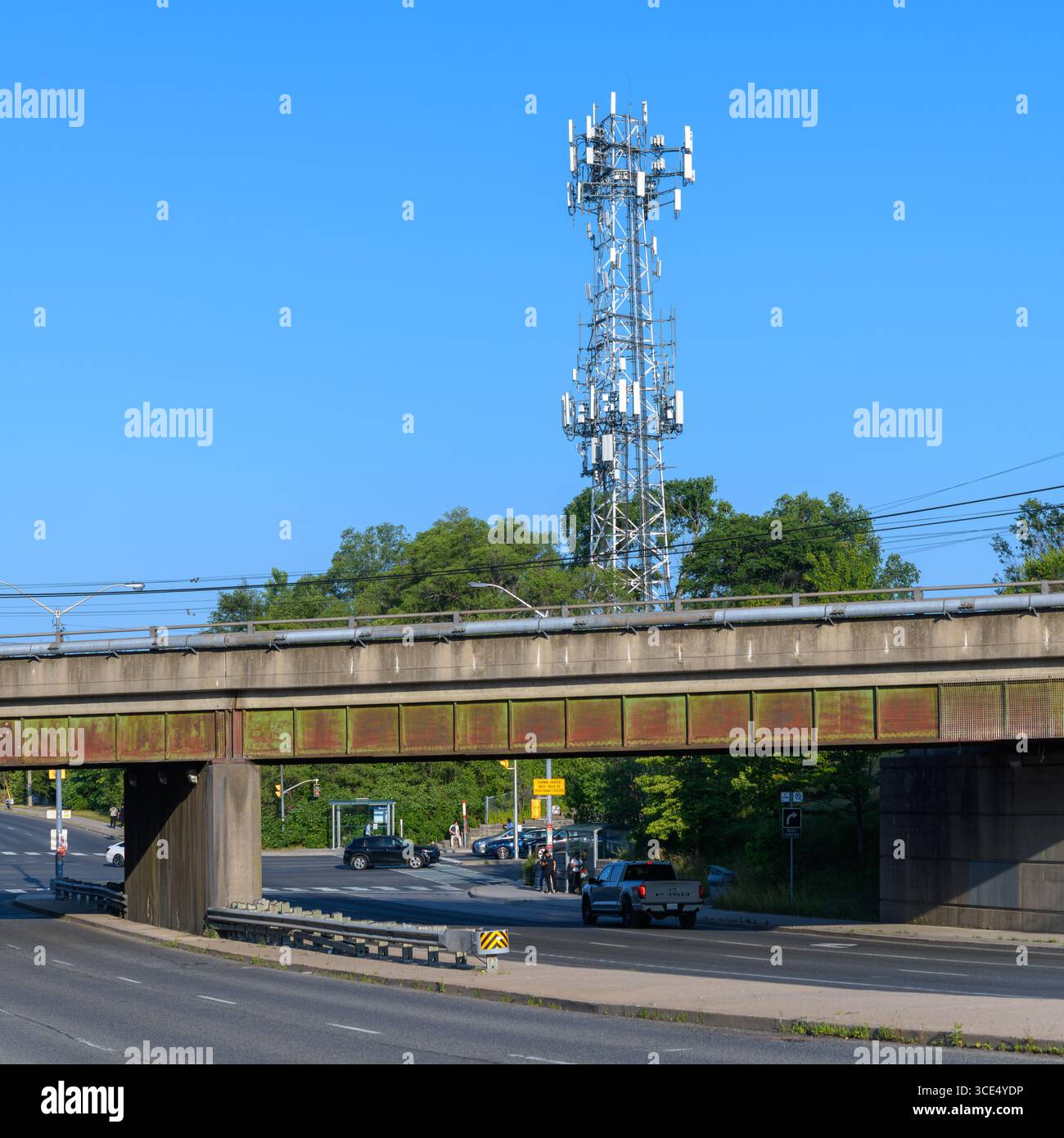 Una torre di celle sorge sopra un ponte ferroviario e un incrocio, con auto che aspettano alla luce e alberi sullo sfondo. Foto Stock