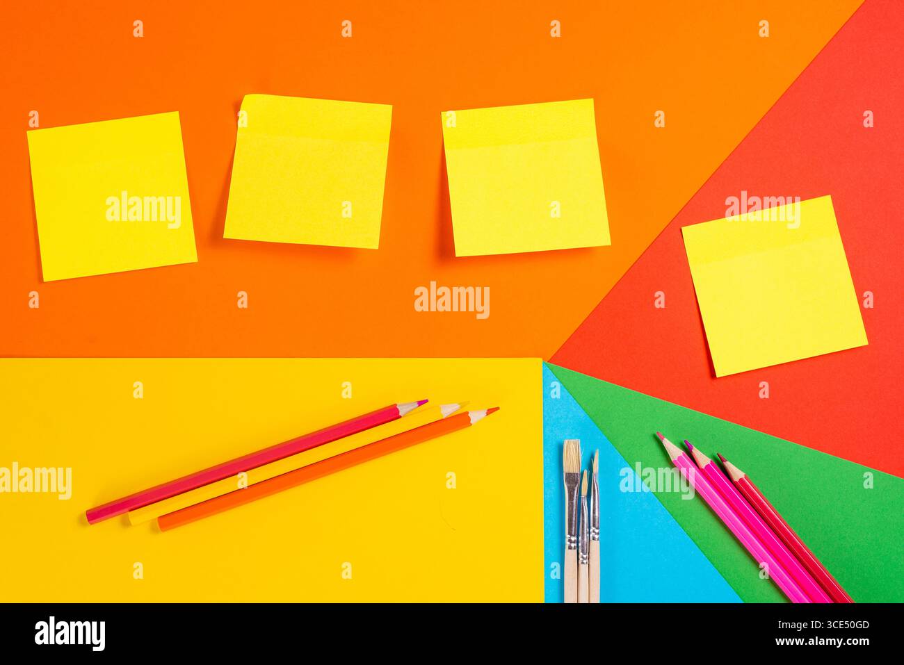 Note adesive, matite e penne disposte su sfondo geometrico colorato. Perfetto per la pianificazione e l'istruzione. Foto Stock