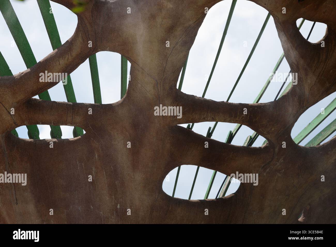 Questa immagine mostra un affascinante dettaglio architettonico caratterizzato da forme organiche e strutture verdi che sbirciano attraverso. Integra perfettamente la natura Foto Stock