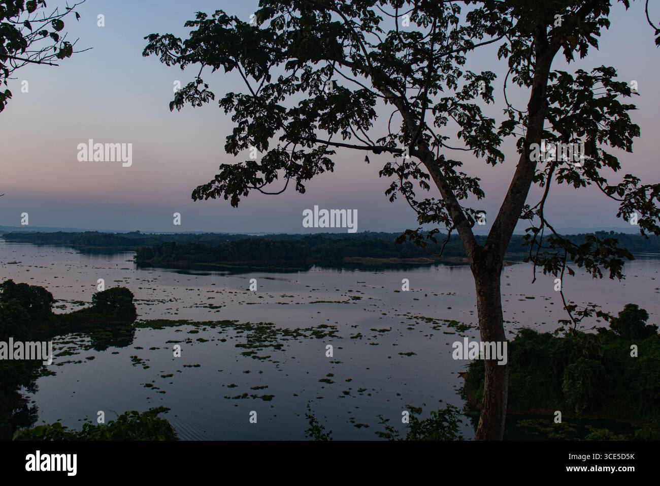 Calmo tramonto al lago Kaptai con acque cristalline che riflettono il sole luminoso e la catena montuosa nebulosa. Foto Stock
