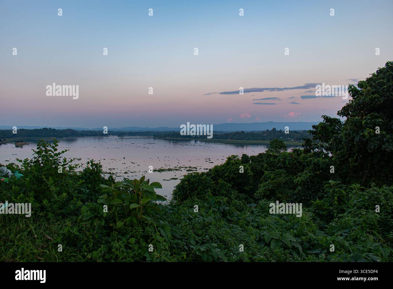 Maestosa scena del tramonto al lago Kaptai con orizzonte luminoso, acqua tranquilla e montagne boscose Foto Stock