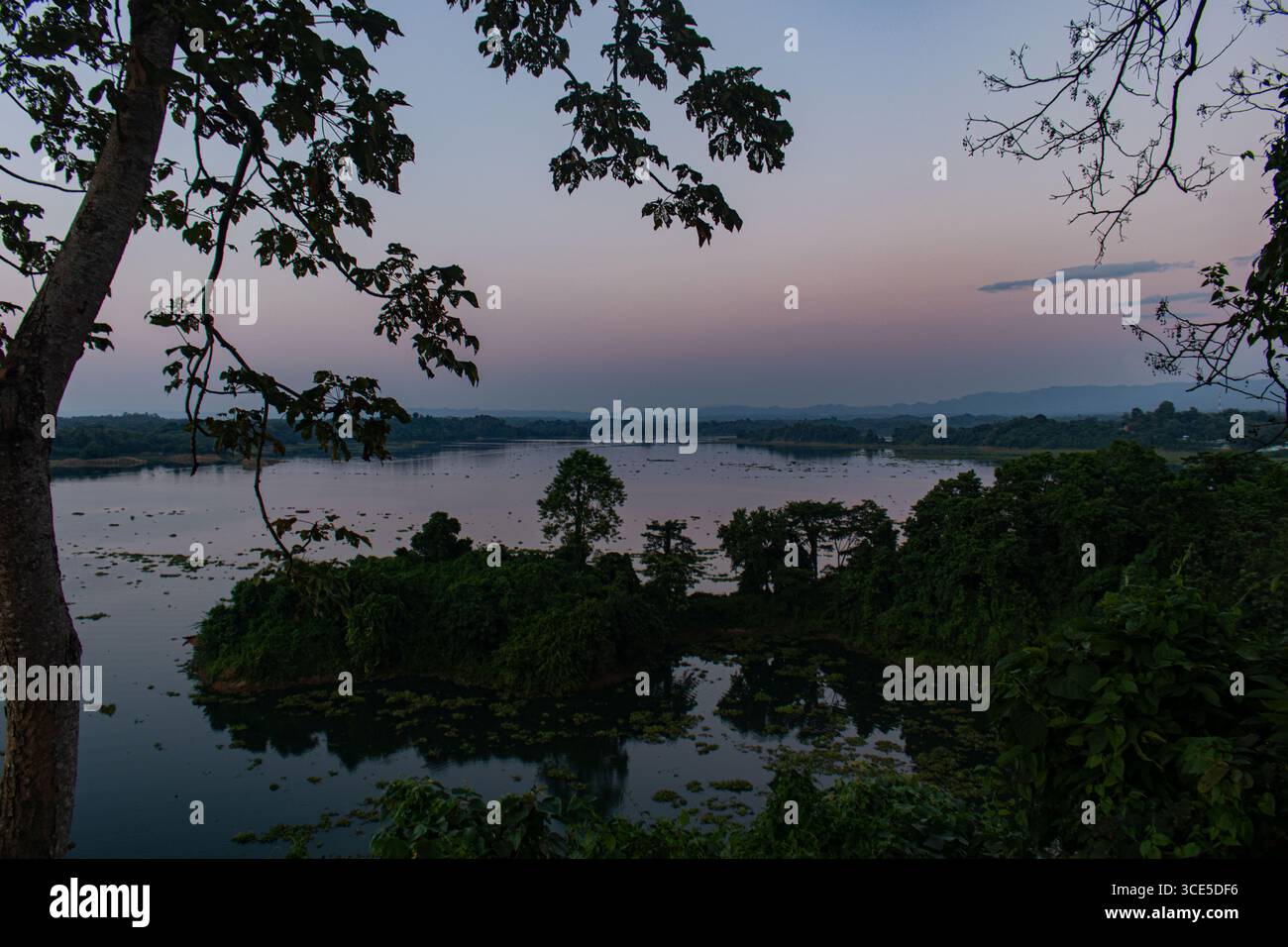 Maestosa e ampia vista sul fiume, circondata da una foresta verde e da un colorato cielo serale al tramonto tranquillo Foto Stock