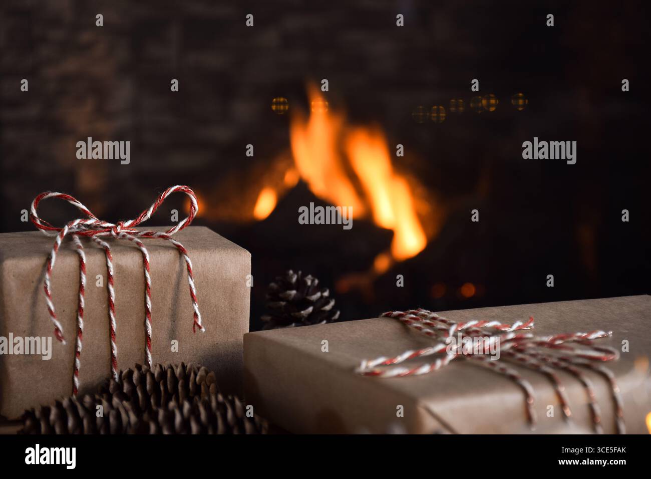Regali di Natale da primo piano avvolti in semplice carta marrone legata con cordoncino rosso e bianco davanti a un caminetto di casa Foto Stock