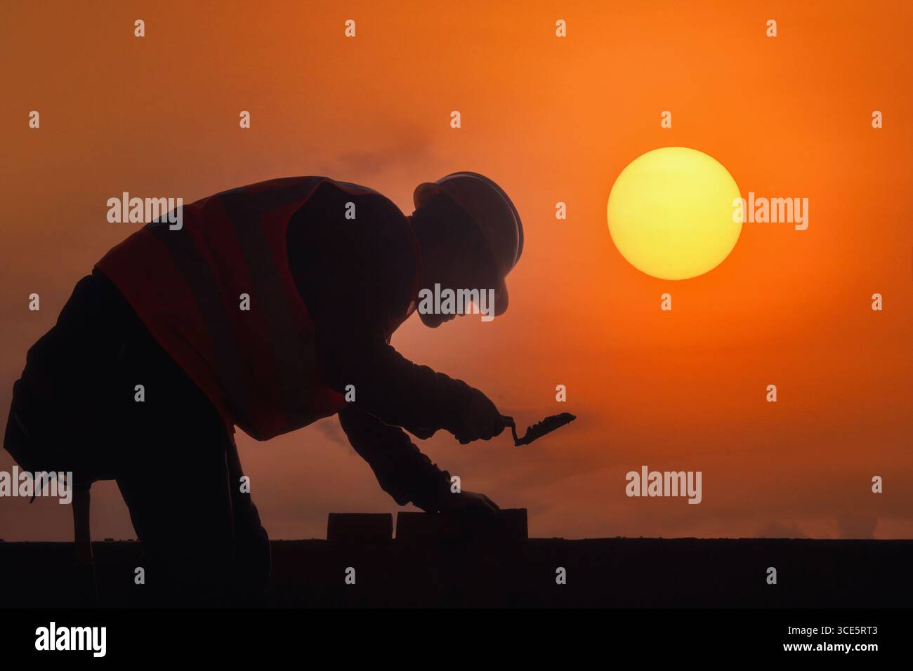 Vista laterale sagoma di un muratore che posa mattoni in un cantiere al tramonto, Thailandia Foto Stock