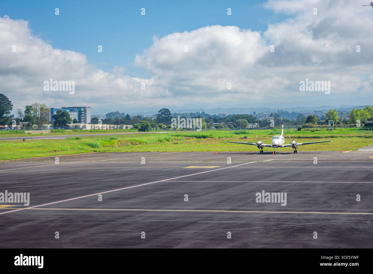 Un piccolo aereo è parcheggiato sulla pista di un aeroporto colombiano con paesaggi verdi e cieli blu sullo sfondo. Foto Stock