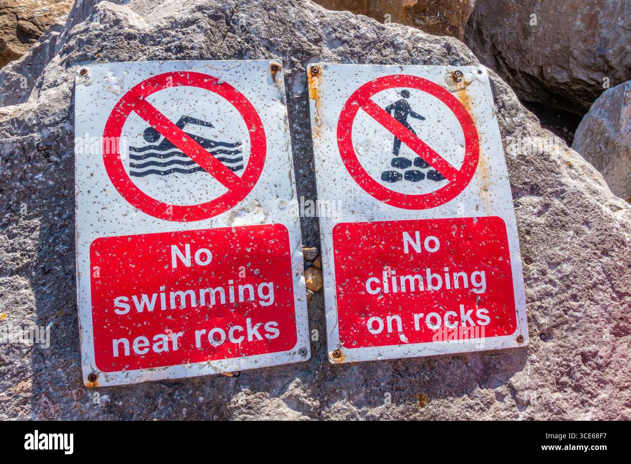 Cartelli segnati dagli agenti atmosferici attaccati a un masso sulla spiaggia di Felixstowe che dicono ai visitatori di non nuotare o arrampicarsi sulle rocce. Foto Stock