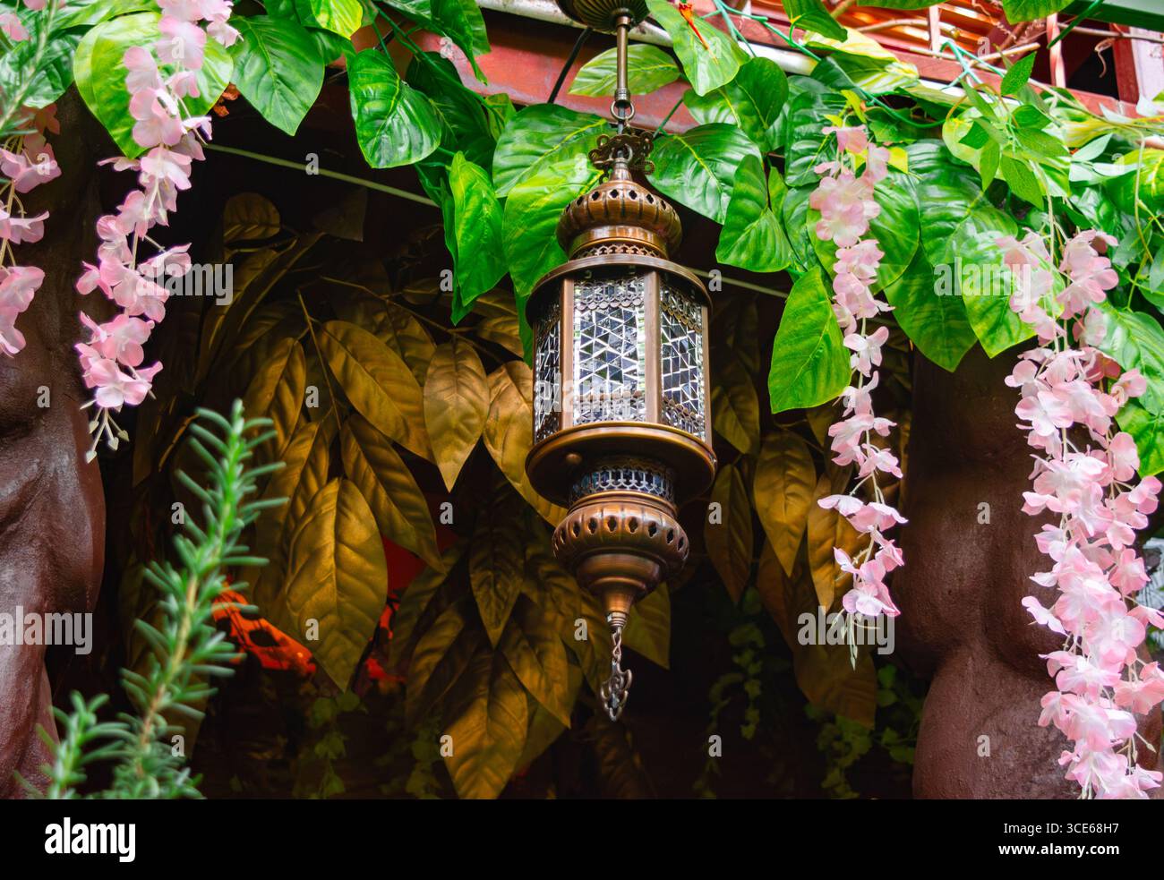 A Villa de Leyva, Boyaca, in Colombia, una lanterna splendidamente lavorata è appesa tra foglie vivaci e fiori rosa. Foto Stock