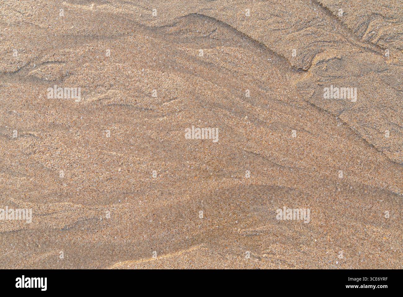 Forme astratte e motivi in sabbia granulosa e acqua fluente sulla spiaggia in una giornata di sole, vista dall'alto. Fondo sabbioso naturale con trama astratta Foto Stock