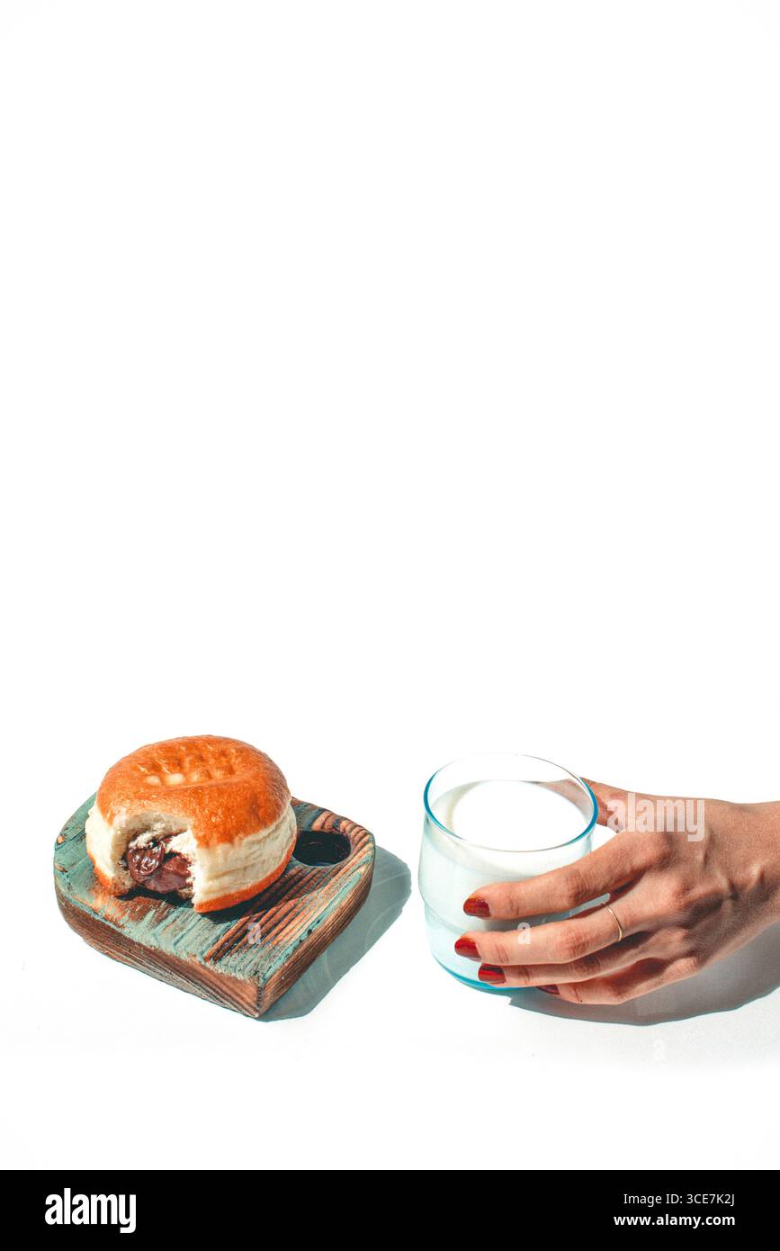 Un bicchiere di latte fresco con una ciambella ripiena di cioccolato; una combinazione classica e deliziosa per iniziare la giornata o godersi una pausa dolce. Foto Stock