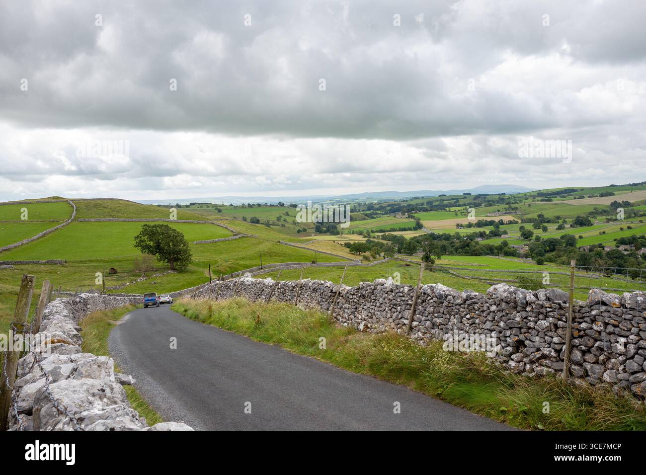 Veicoli che percorrono la ripida discesa stretta Cove Road con muretti a secco in pietra calcarea, Malham, Yorkshire Dales, Inghilterra, Regno Unito. Foto Stock
