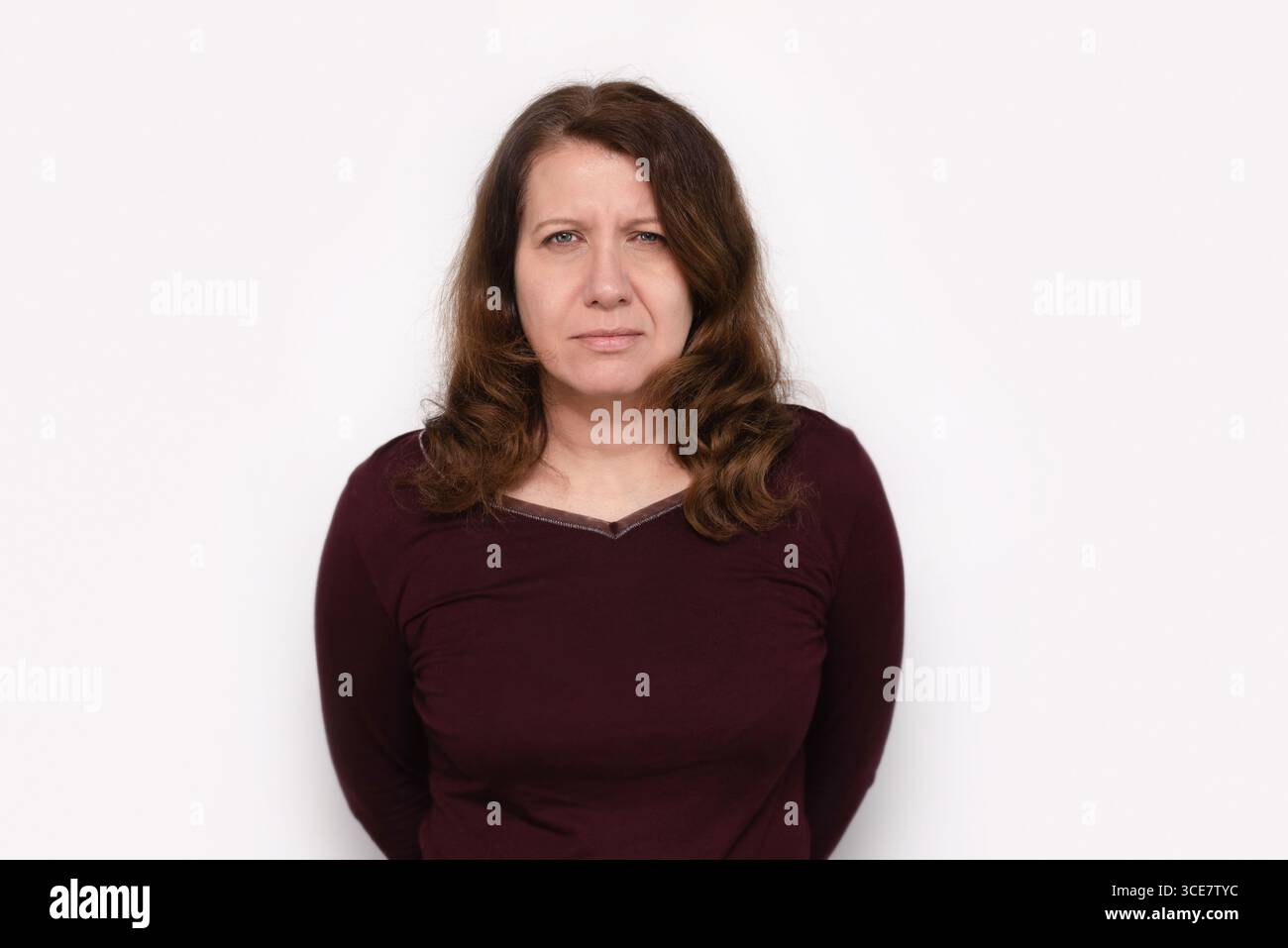 Una donna seria che indossa un top color marrone marrone si trova su uno sfondo bianco sfumato. La sua espressione trasmette determinazione, meditazione Foto Stock