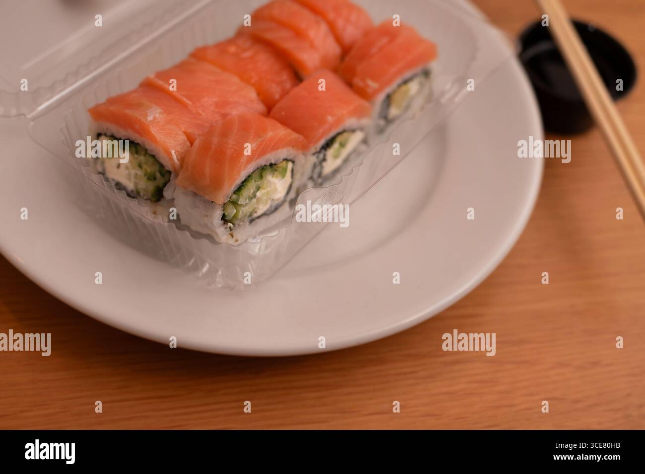 Sushi al salmone preparati al momento disposti su un piatto bianco, accompagnati da bacchette e un lato di salsa da immersione su uno sfondo di legno Foto Stock