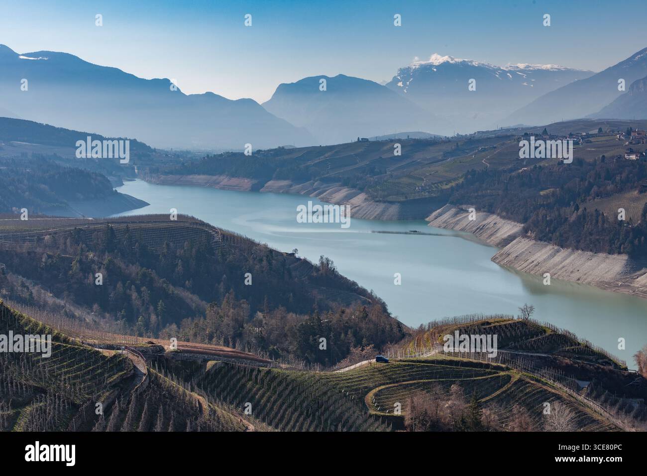 Vista panoramica sul lago artificiale di Santa Giustina, creato da una diga in Val di non, in Trentino, circondata da vigneti terrazzati e da un monte innevato Foto Stock