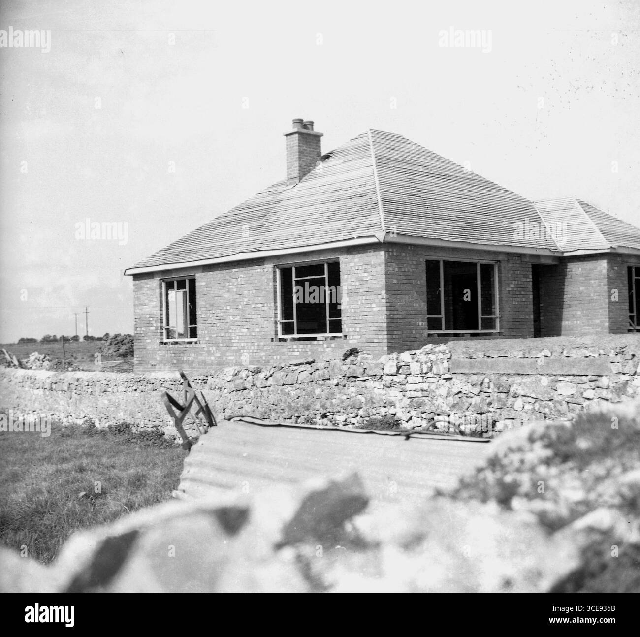Anni '1950, storico, su terreni agricoli rurali, un nuovo bungalow in costruzione, Inghilterra, Regno Unito. La casa a un piano attende che le piastrelle vadano su un tetto a falde di legno appena posato. Foto Stock