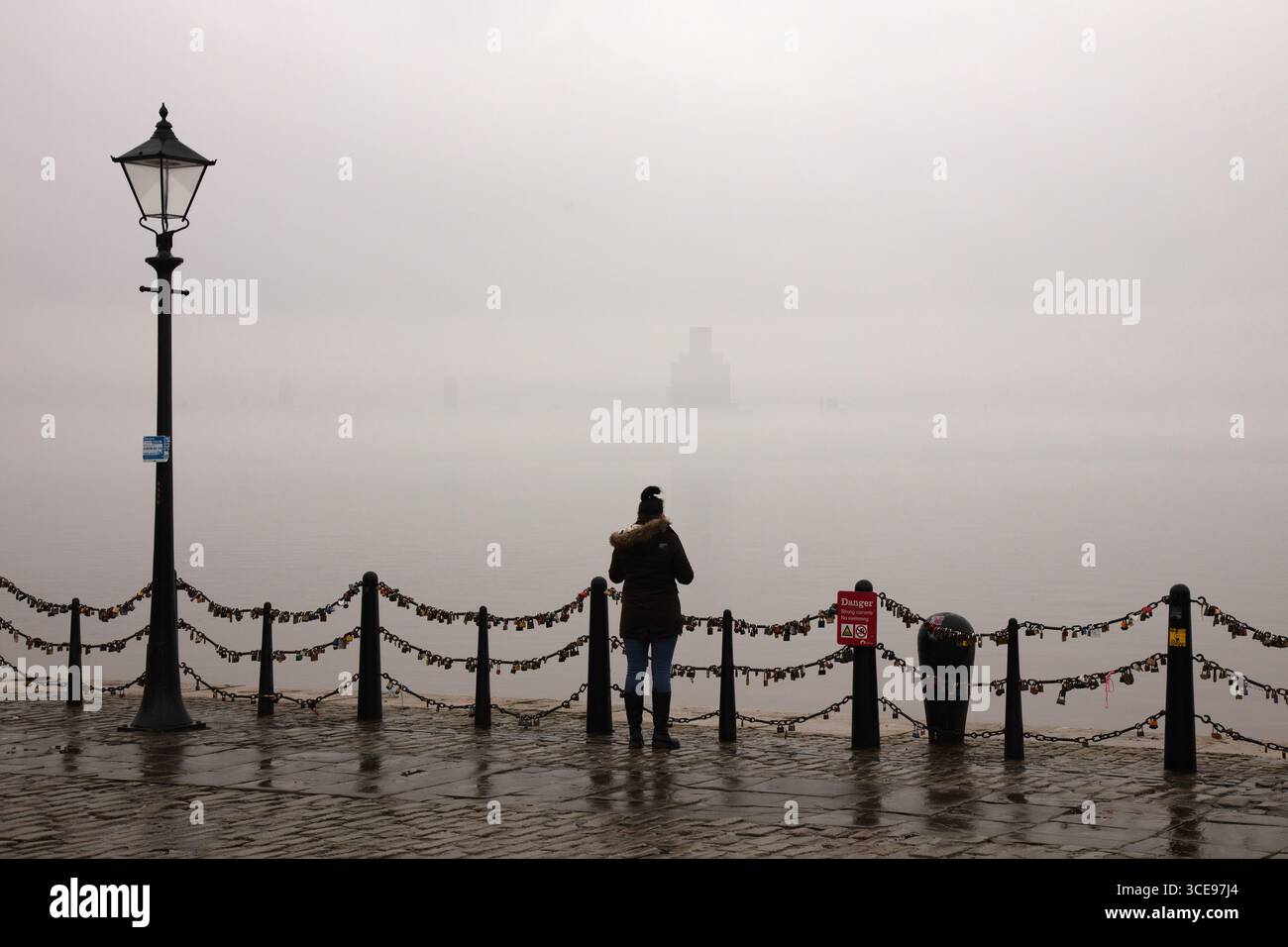 Donna in piedi contro la ferrovia sul lungomare di Liverpool a Fog, Albert Dock Foto Stock