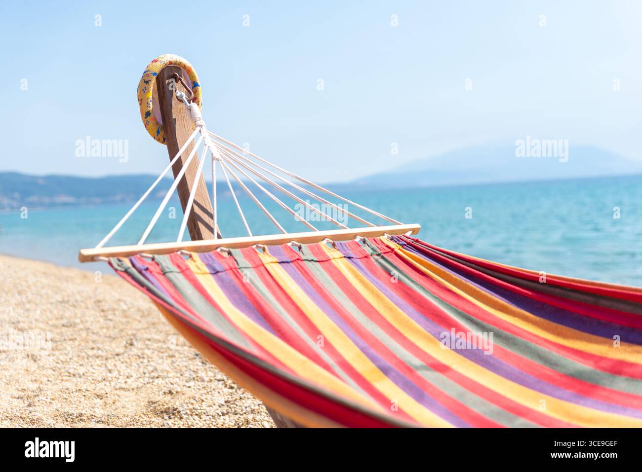 Amaca a righe sulla spiaggia di ciottoli in riva al mare calmo, perfetta per il relax estivo e le vacanze al mare Foto Stock