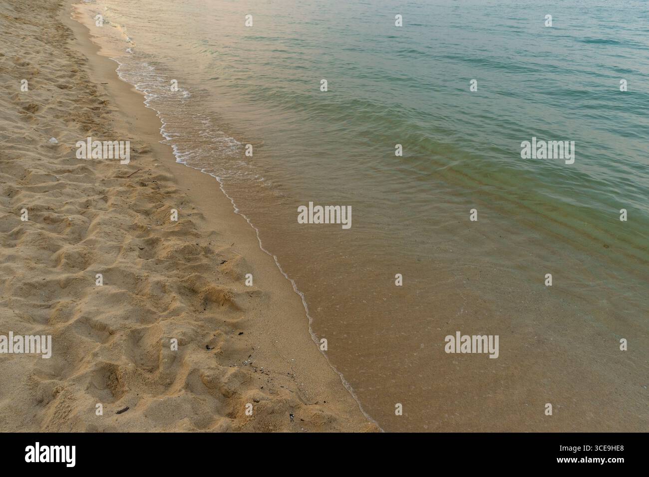 Vista sul litorale con spiaggia sabbiosa che incontra il mare turchese sotto il cielo serale Foto Stock