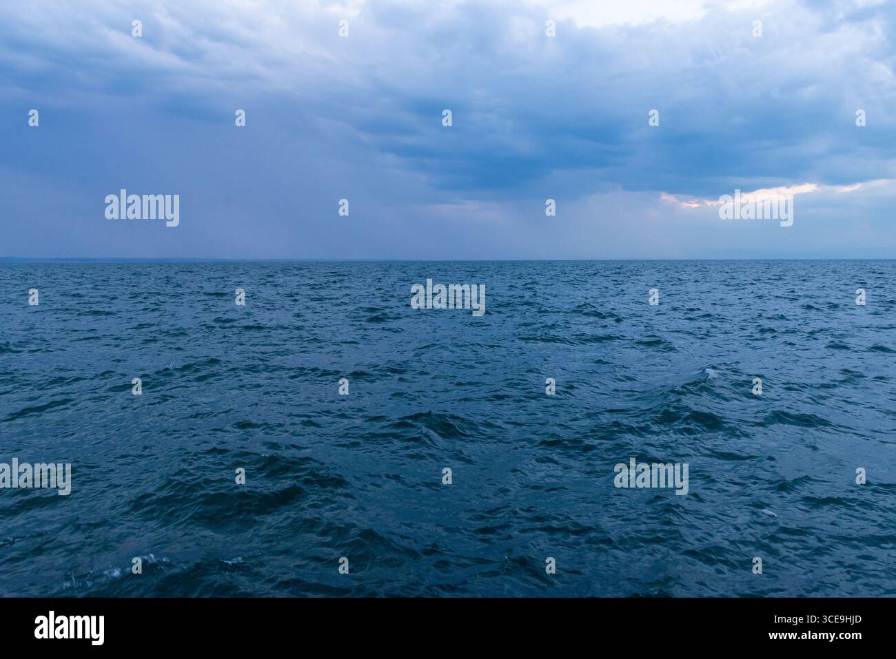 Oceano blu sotto il cielo nuvoloso con pioggia lontana all'orizzonte, perfetto per il clima, i viaggi o gli sfondi di avventura Foto Stock