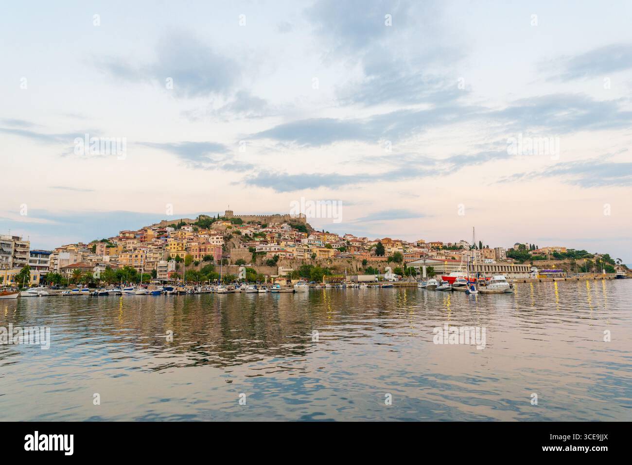 Foto grandangolare della città vecchia di Kavala e della fortezza che si innalza sopra la baia, con case tradizionali e acque blu calme Foto Stock