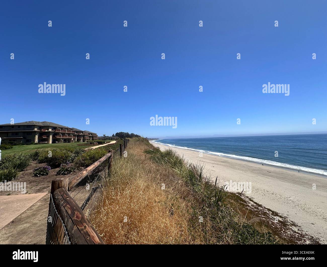 Una vista panoramica della costa da un promontorio, che mostra dune erbose, case fronte oceano e un lungo tratto di spiaggia sabbiosa che incontra le calme acque blu Foto Stock