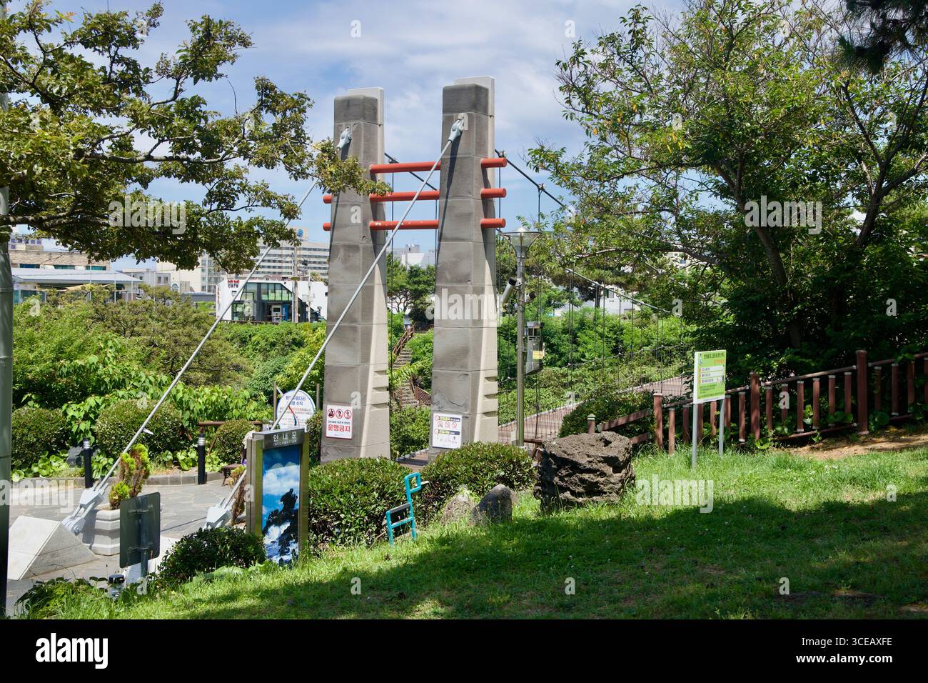 Tralicci e cavi di cemento segnano l'ingresso al ponte nuvola di Yongyeon nella città di Jeju, adagiato tra alberi con segnaletica per il parco e sentieri nelle vicinanze. Foto Stock