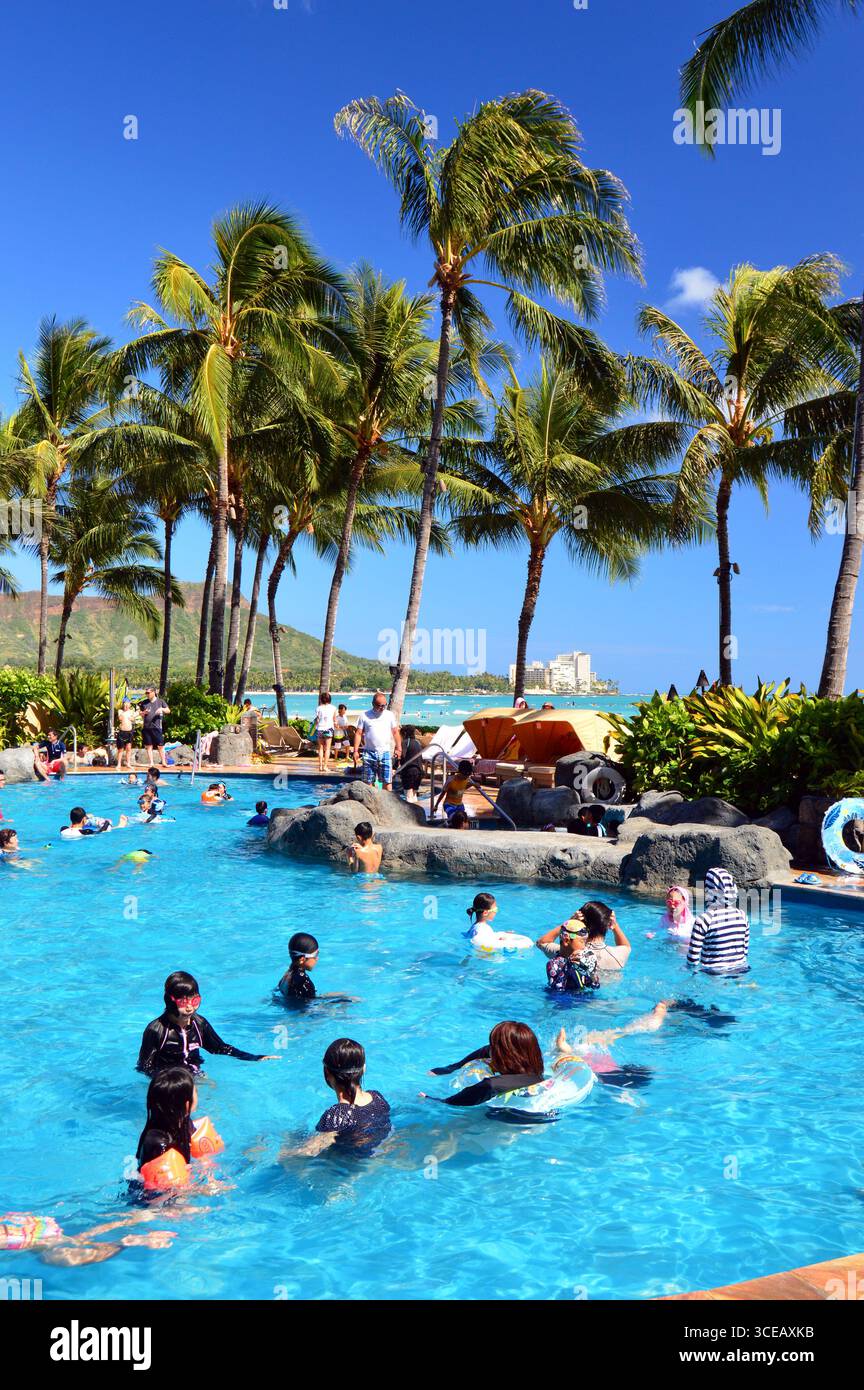 Un gruppo di turisti si rilassa nuotando in una piscina in un resort di vacanza sulla riva di Waikiki Beach, Hawaii Foto Stock