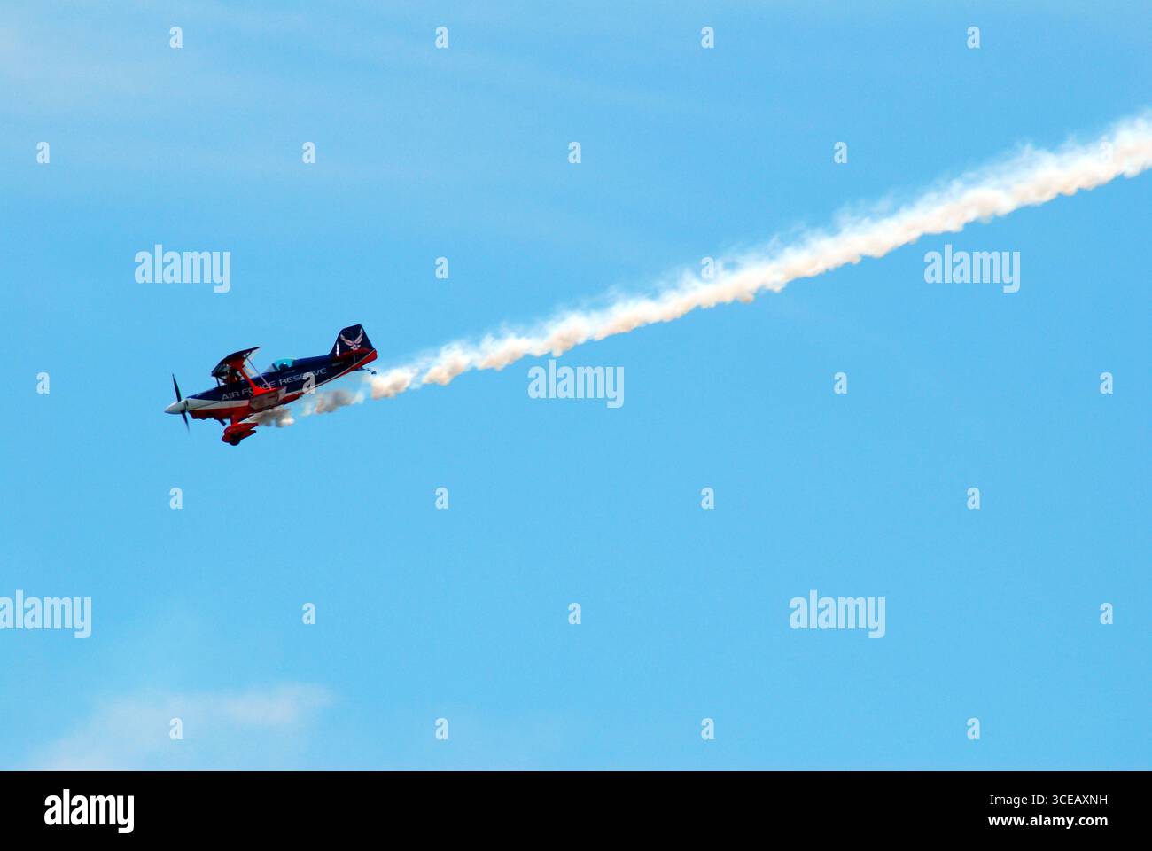 Un pilota di acrobazie vola il suo biplano attraverso il cielo mentre una linea di fumo corre dietro l'aereo Foto Stock