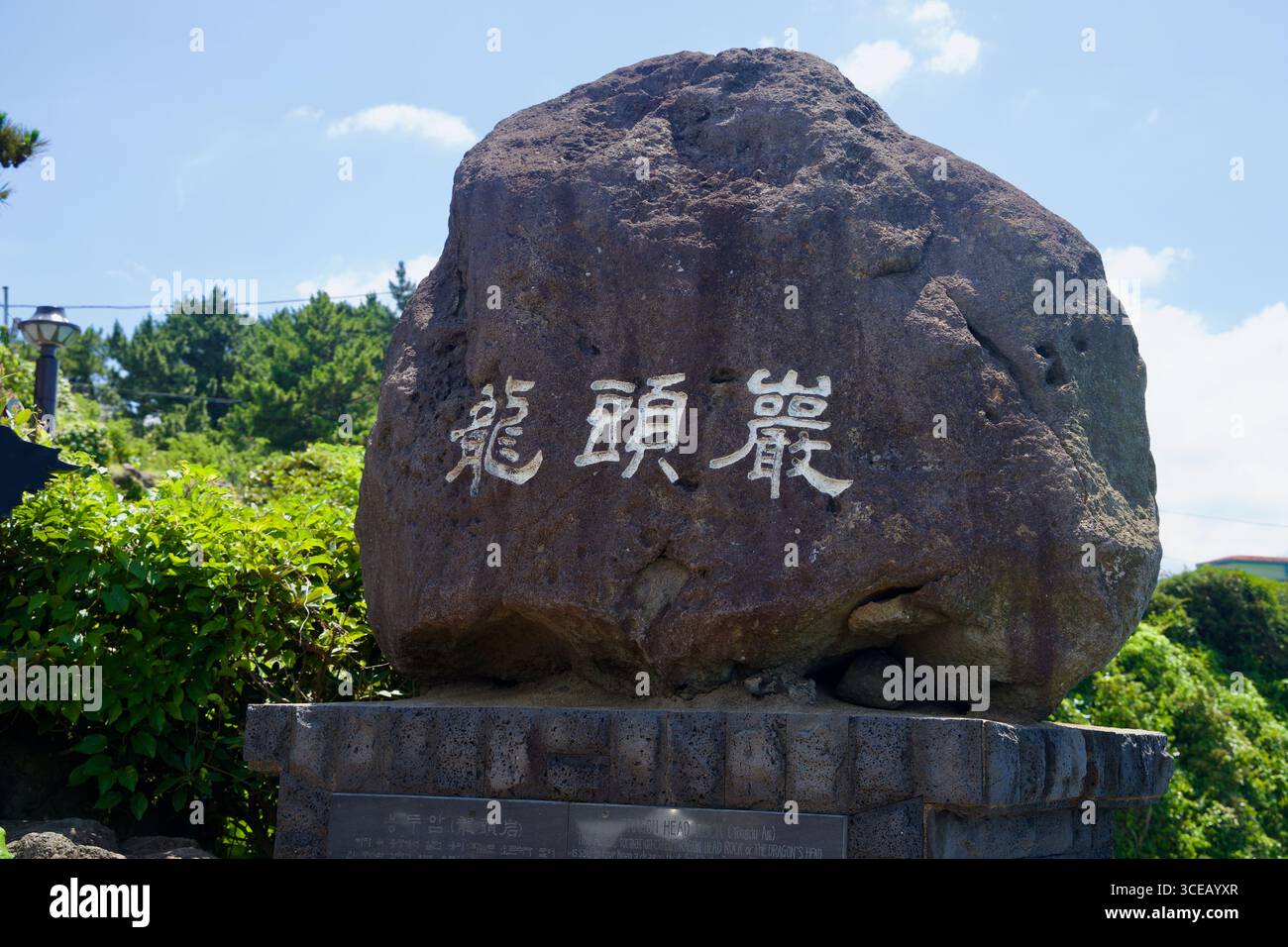 Un masso intagliato che porta i caratteri tradizionali di Yongduam si erge all'ingresso che si affaccia, incorniciato dal verde e dal cielo estivo nella città di Jeju. Foto Stock