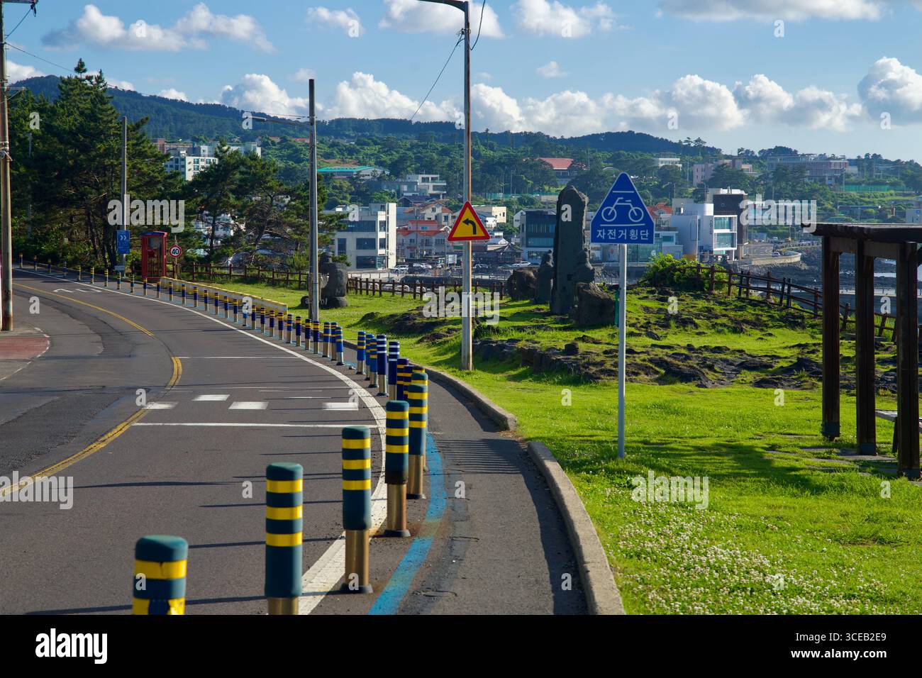 Nei pressi del Darak Shelter, una pista ciclabile segnata parallelamente alla strada costiera, oltre i cartelli e un piccolo padiglione sopra la prateria vulcanica, con il lungomare di Aewol Foto Stock