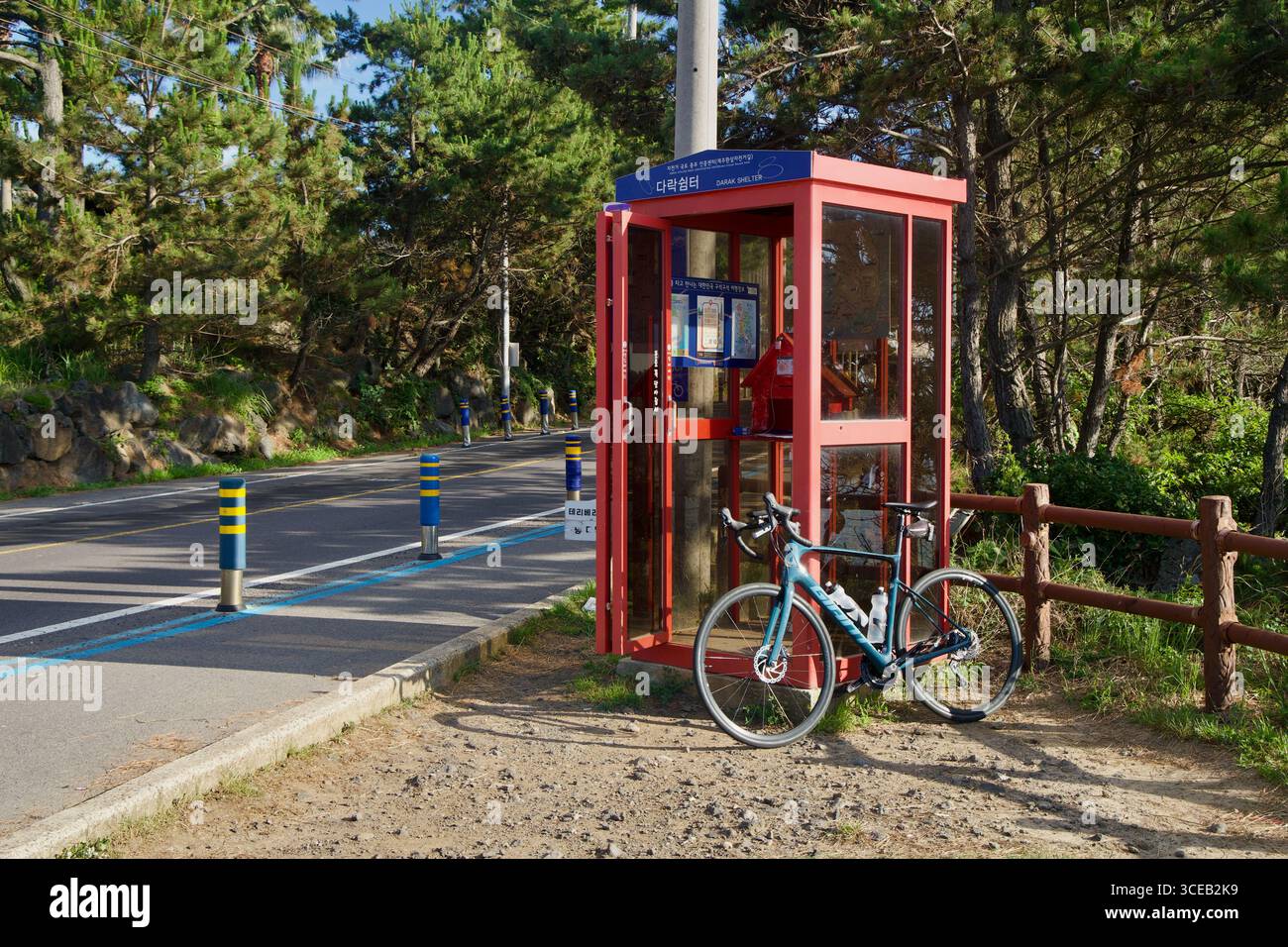 Vista sulla strada dello stand di certificazione Darak Shelter accanto alla pista ciclabile segnalata e ai pini, con una bicicletta parcheggiata davanti. Foto Stock
