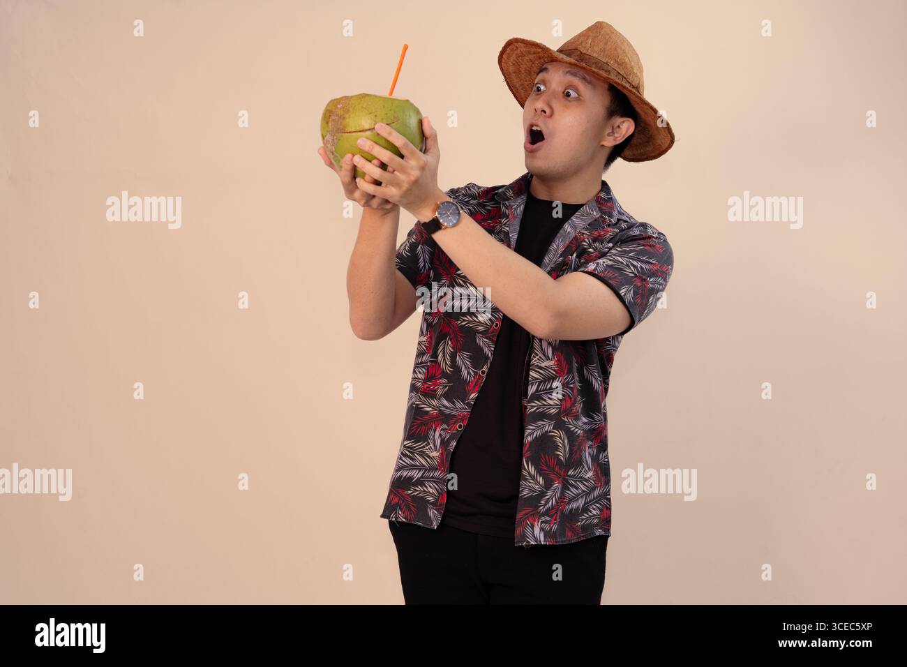 uomo in camicia stampata che regge noce di cocco con paglia arancione e indossa un cappello di paglia Foto Stock