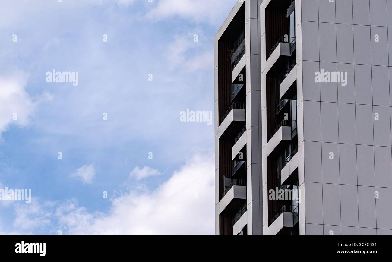 Alto e moderno edificio che presenta un elegante design architettonico con grandi finestre ed elementi a contrasto, adagiato su un vivace cielo blu con sca Foto Stock