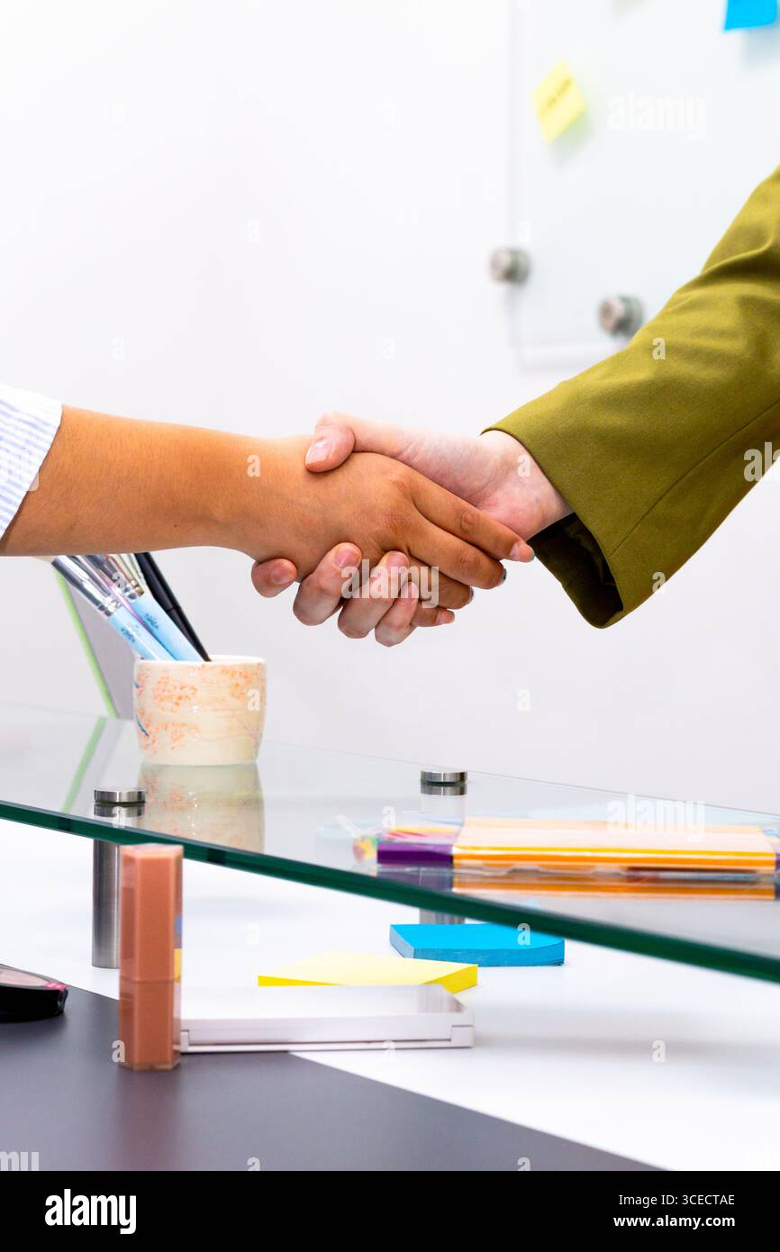Primo piano di una stretta di mano tra due professionisti su un tavolo di vetro, che simboleggia il successo di una negoziazione o di una partnership, in un ambiente di ufficio moderno Foto Stock