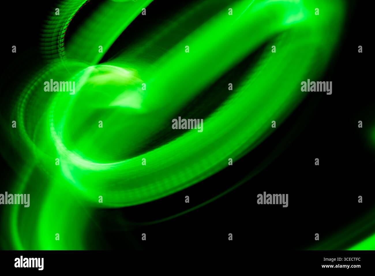 Un'immagine astratta dinamica con vorticose tracce di luce verde su sfondo scuro. Il bagliore simile al neon crea un senso di movimento ed energia, perfec Foto Stock