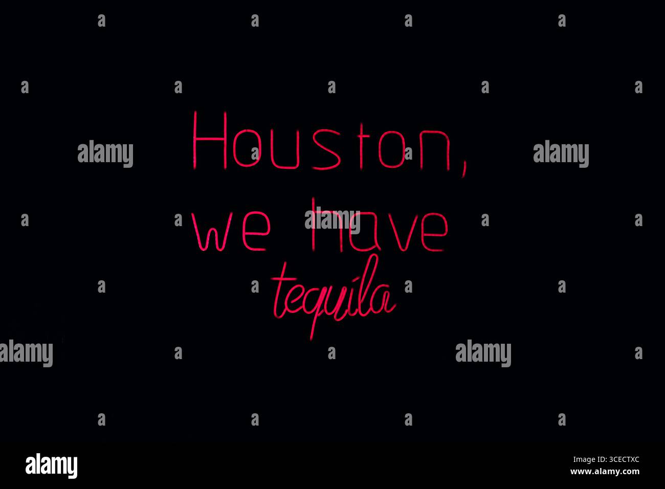 Un cartello al neon mostra la frase umoristica Houston, abbiamo tequila su uno sfondo scuro. Il tocco giocoso di una famosa citazione aggiunge un tocco stravagante Foto Stock