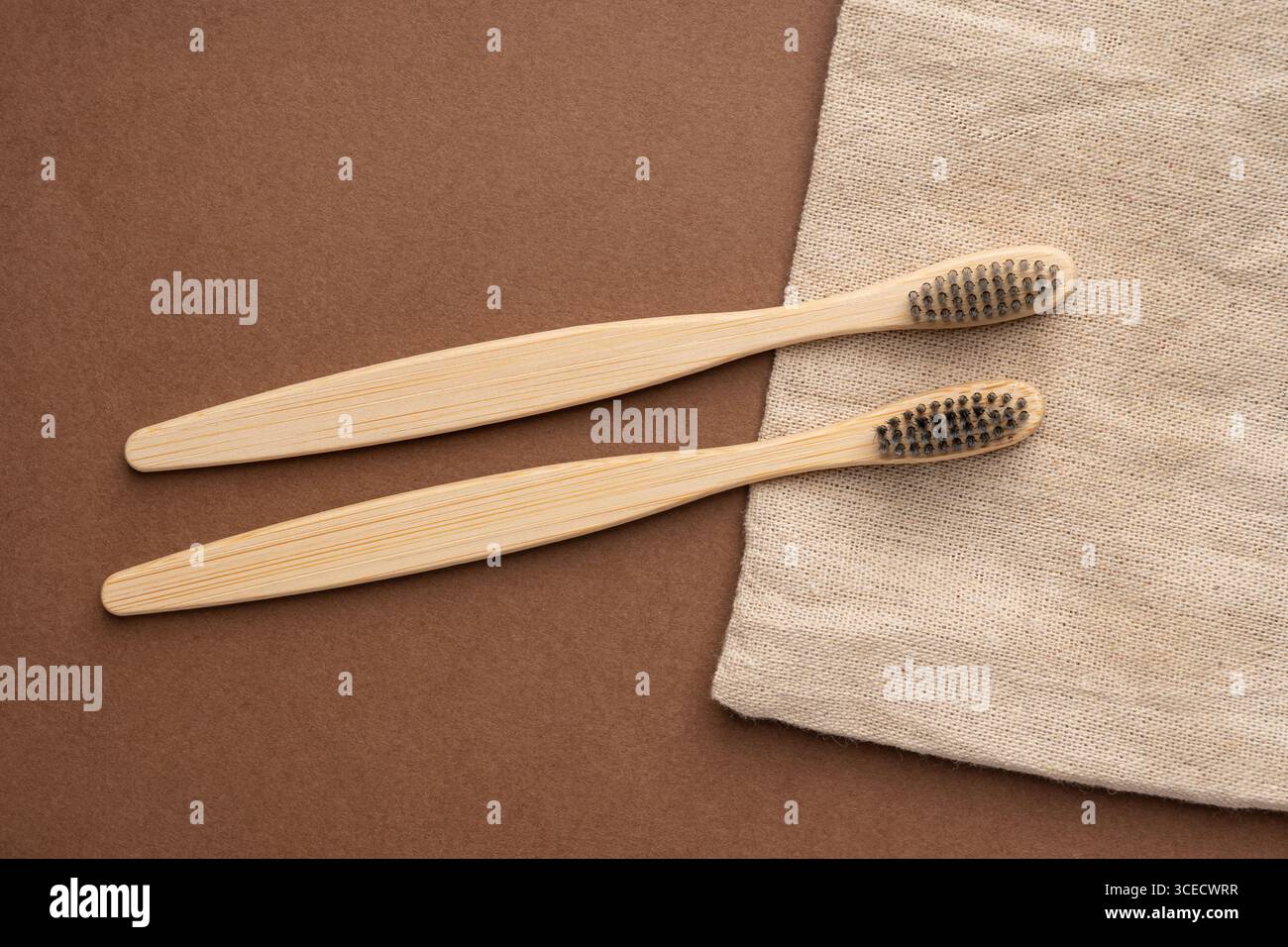 Vista dall'alto di due spazzolini da denti in bambù su una superficie marrone, accompagnati da un tessuto beige naturale, che enfatizza i prodotti da bagno ecologici e sostenibili. Foto Stock