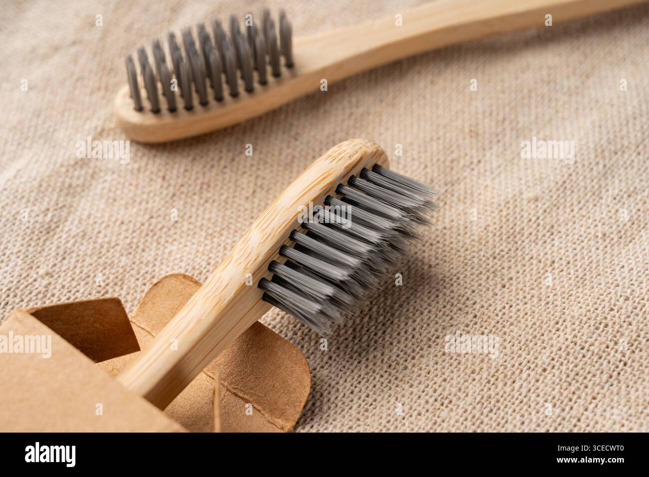 Vista dall'alto degli spazzolini in bambù con setole morbide su un tessuto beige testurizzato. Il design ecosostenibile e confezionato enfatizza l'eliminazione degli sprechi Foto Stock