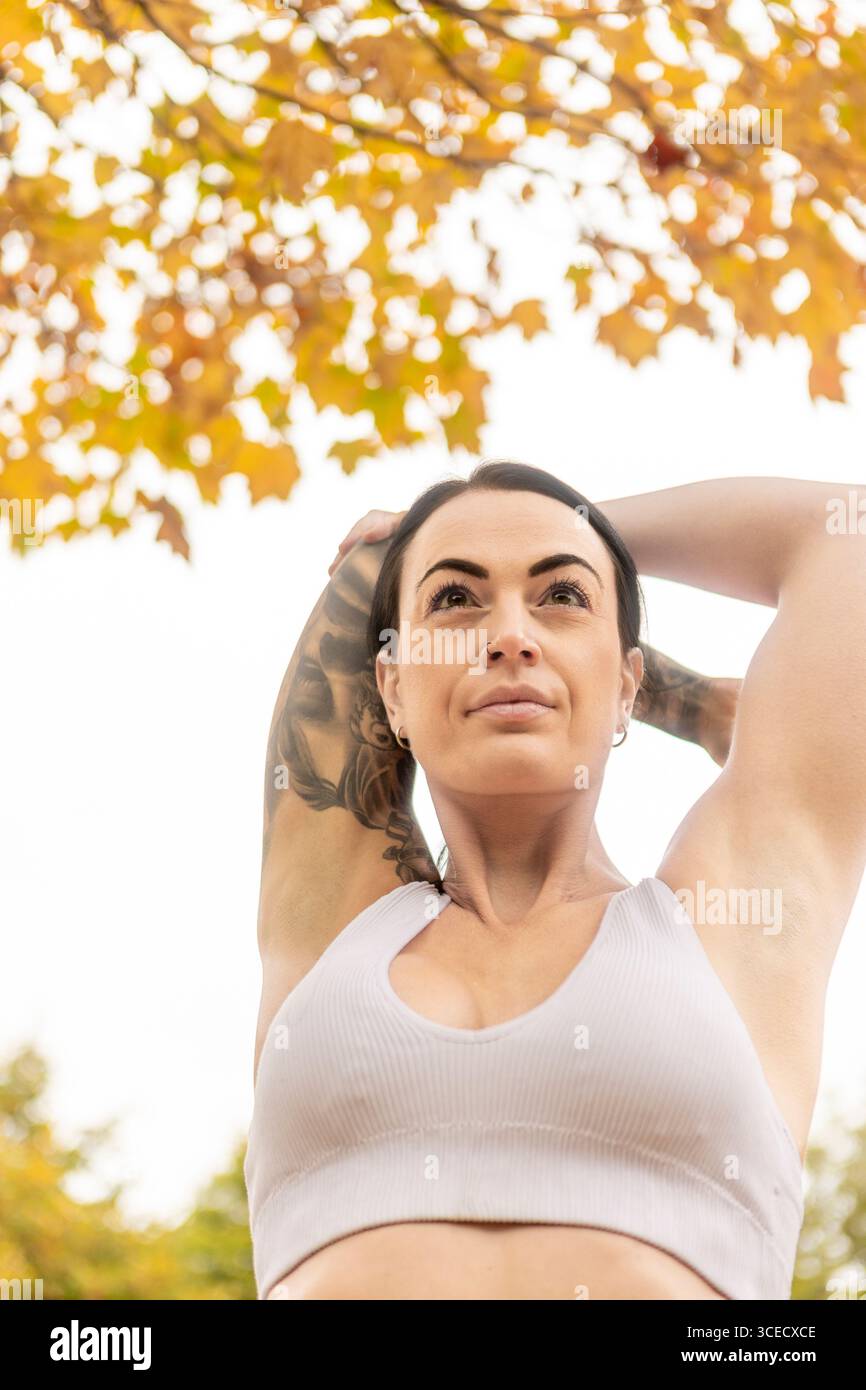 Una donna allunga le braccia mentre si esercita all'aperto in autunno in un parco neozelandese. Il vivace fogliame autunnale aggiunge uno sfondo scenico al suo lavoro Foto Stock