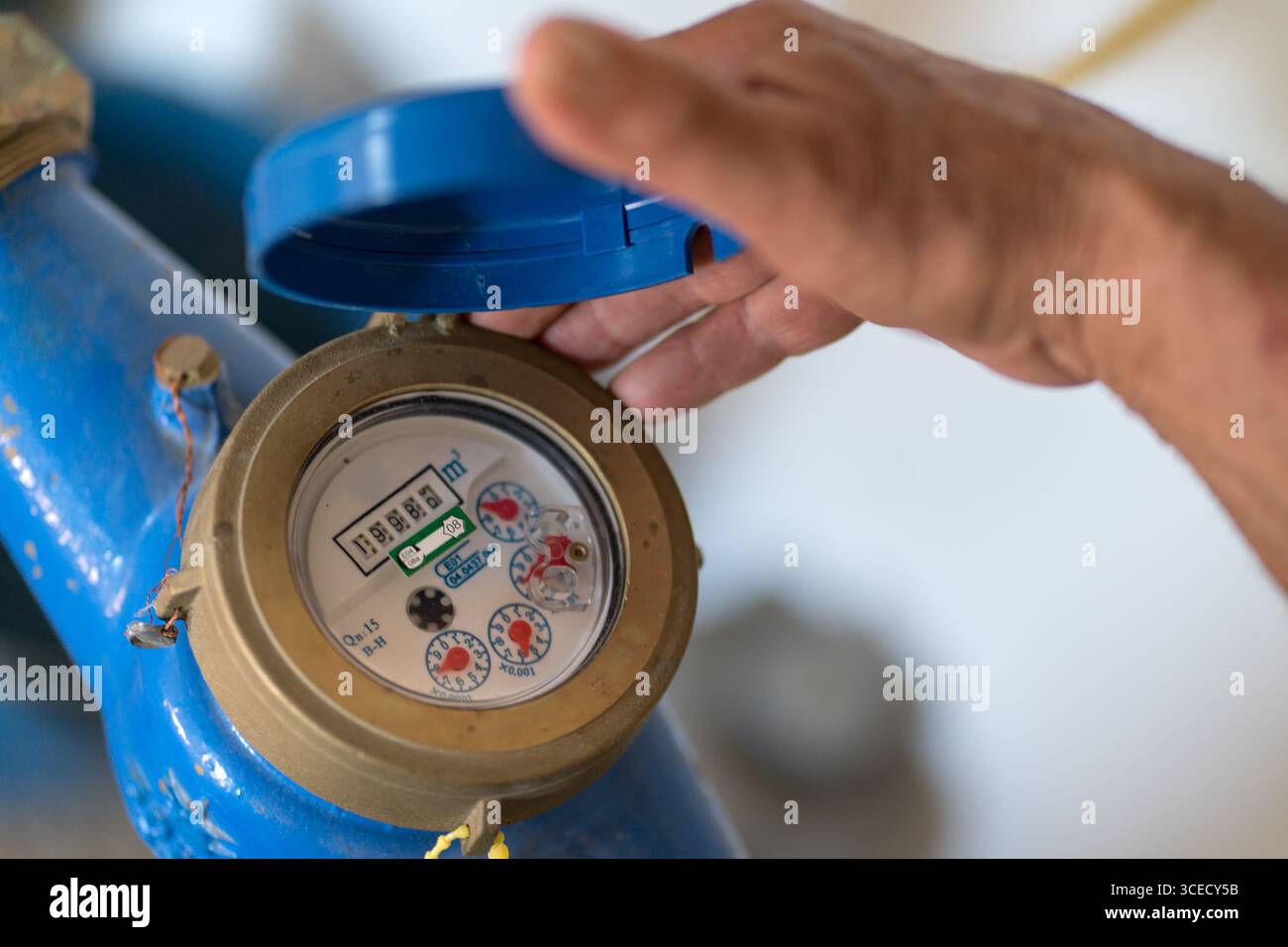 Un anziano corto e irriconoscibile ispeziona un contatore dell'acqua, regolando la copertura protettiva blu. Le sue mani rivelano anni di esperienza, catturando una momen Foto Stock