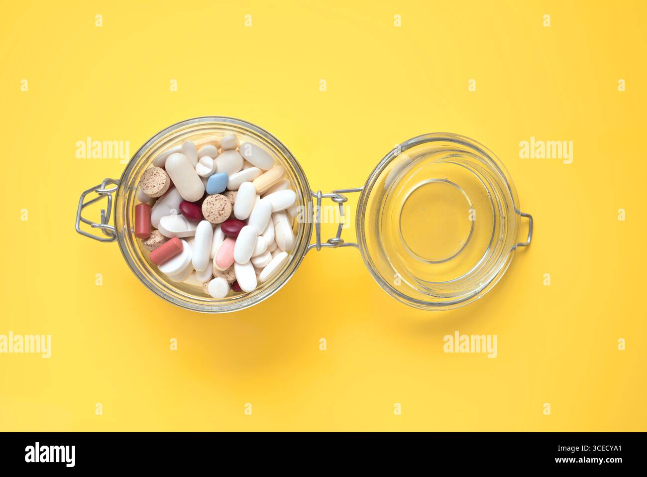 Un ampio vaso in vetro con imboccatura pieno di pillole assortite si apre su uno sfondo giallo brillante. La varietà colorata delle pillole crea una strikin Foto Stock