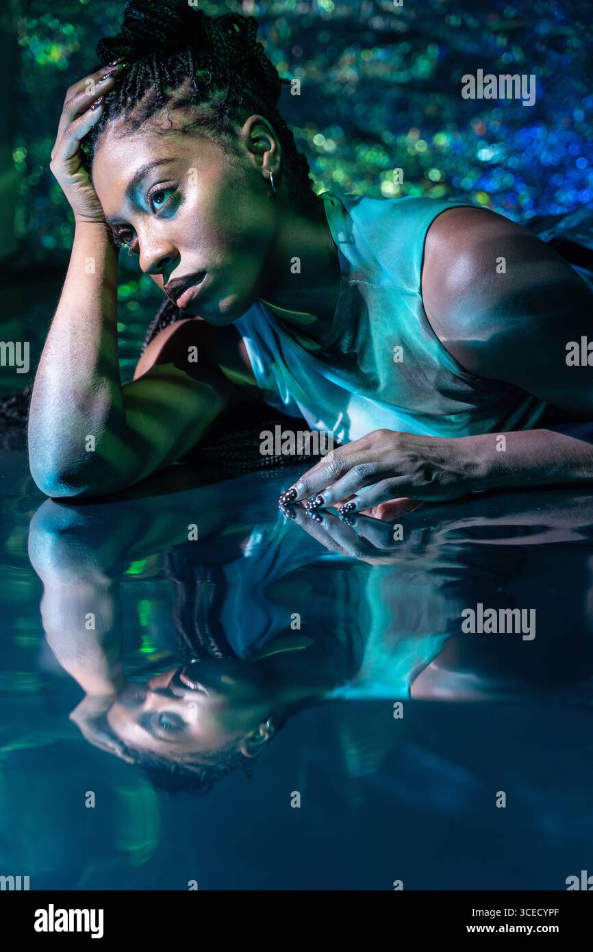 Una giovane donna africana futuristica si rilassa in un paesaggio metaverso digitale, circondato da colori brillanti. La sua espressione è premurosa, incarna inno Foto Stock