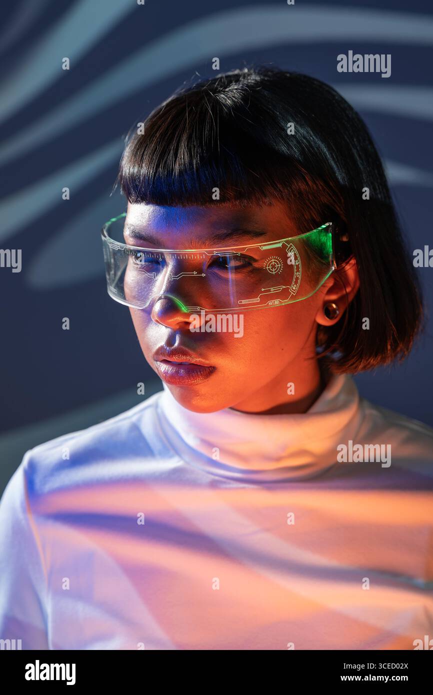 Una donna latina esplora un mondo digitale coinvolgente utilizzando innovativi occhiali per realtà virtuale, indossando un dolcevita bianco con un'illuminazione al neon suggestiva Foto Stock