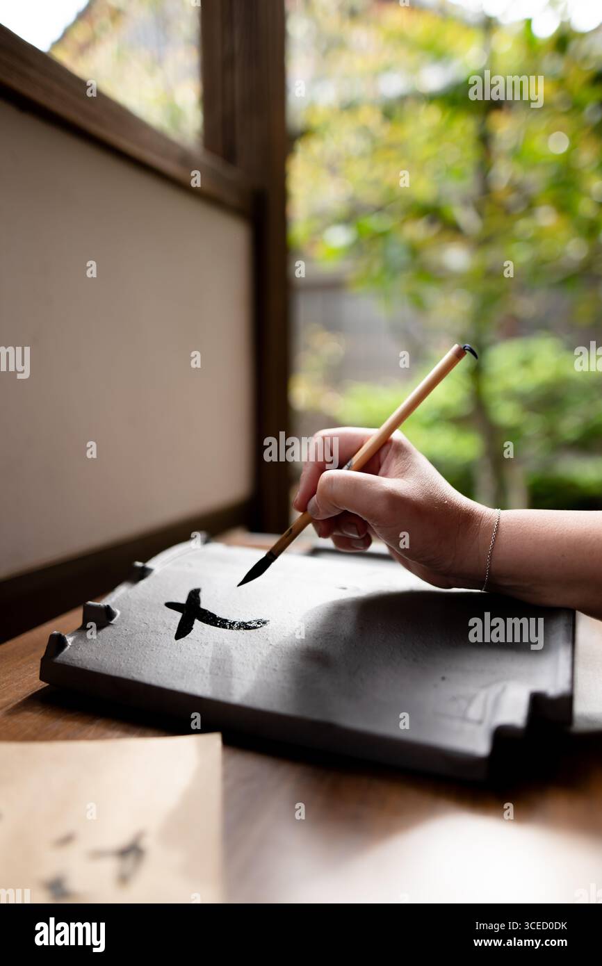 Primo piano di una mano che usa un pennello per praticare la calligrafia giapponese su una tradizionale pietra a inchiostro al Ninna-ji di Kyoto, Giappone, catturando l'essenza di t Foto Stock