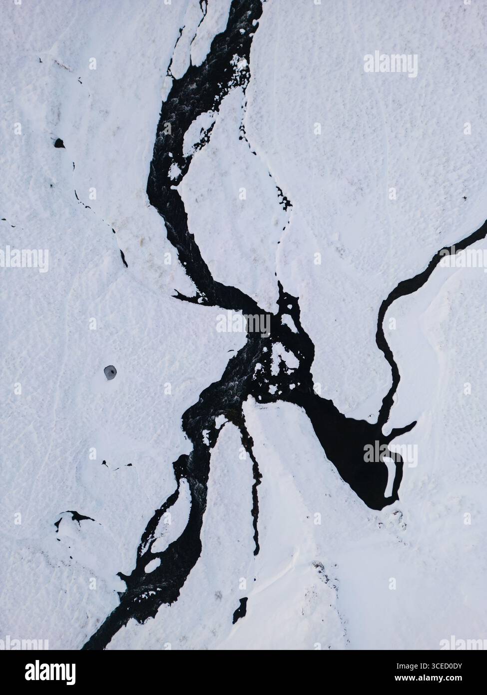 Vista aerea dell'Islanda in inverno, con un paesaggio ghiacciato. La neve ricopre il terreno, mentre i fiumi bui e tortuosi tagliano attraverso il bianco incontaminato. Foto Stock
