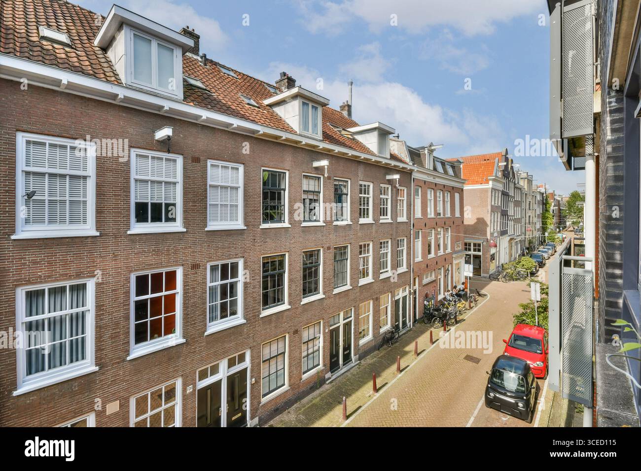 Una vista pittoresca di una strada residenziale di Amsterdam caratterizzata da un'architettura classica, fiancheggiata da biciclette e auto parcheggiate sotto un cielo azzurro. Foto Stock