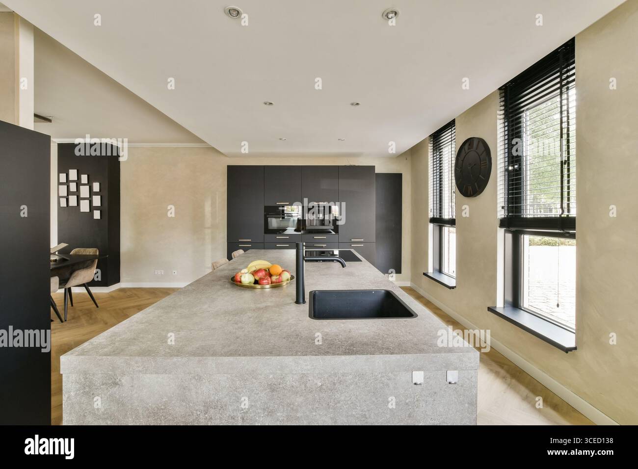 Una cucina elegante e contemporanea con un'isola, elettrodomestici moderni e un design minimalista con illuminazione naturale e pavimenti in legno. Foto Stock