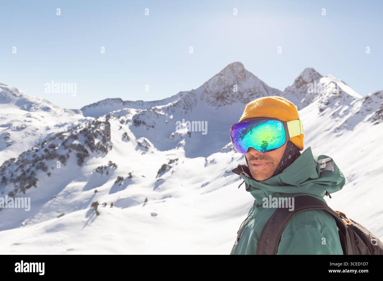Uno snowboarder vestito con l'equipaggiamento invernale si trova in un ambiente montano di campagna. La luce del sole esalta il paesaggio innevato, ideale per una vacanza libera Foto Stock