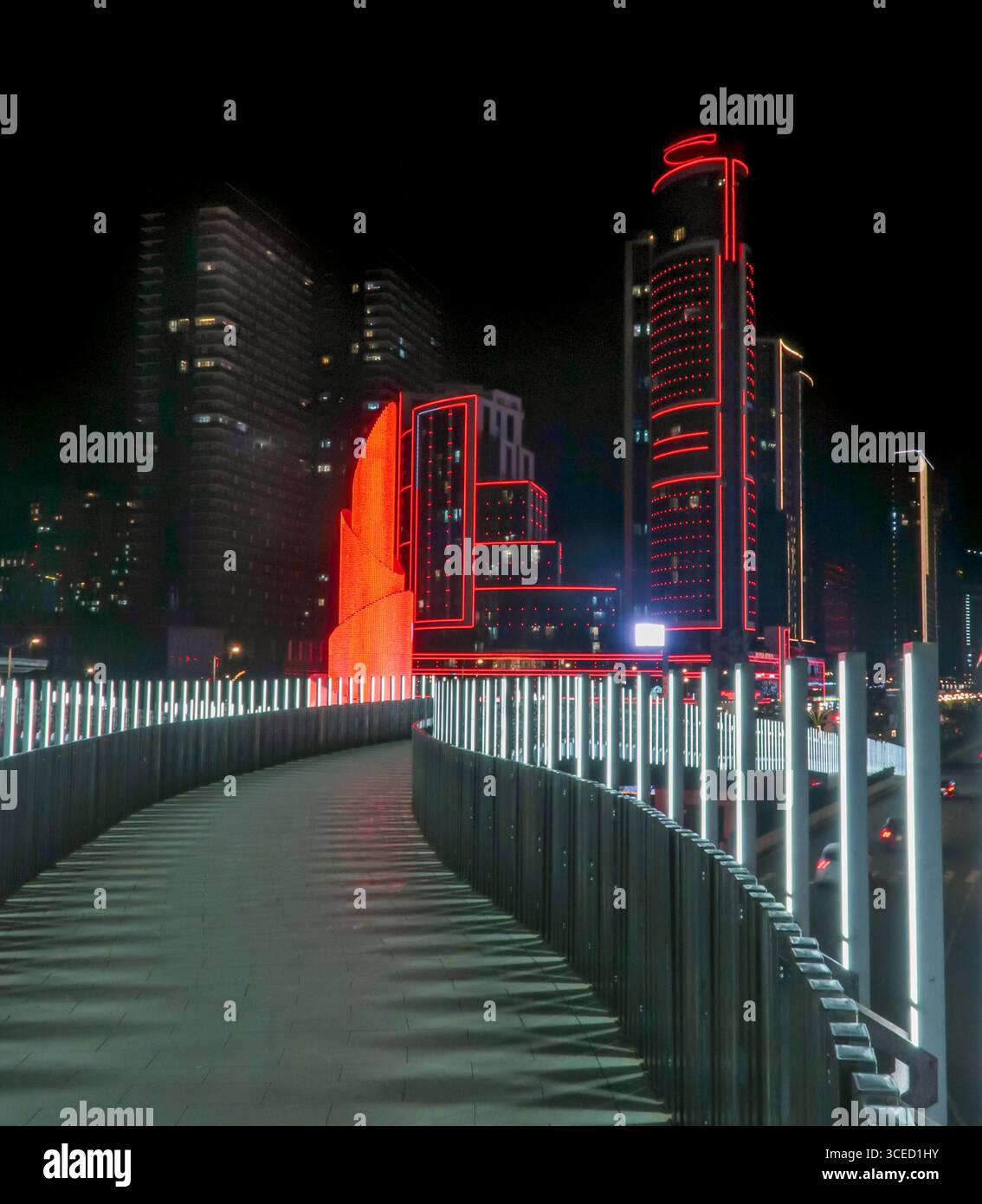 Vista notturna di un moderno paesaggio urbano in Georgia, caratterizzato da un grattacielo illuminato e adornato da luci rosse. Un vialetto futuristico con rampe luccicanti Foto Stock